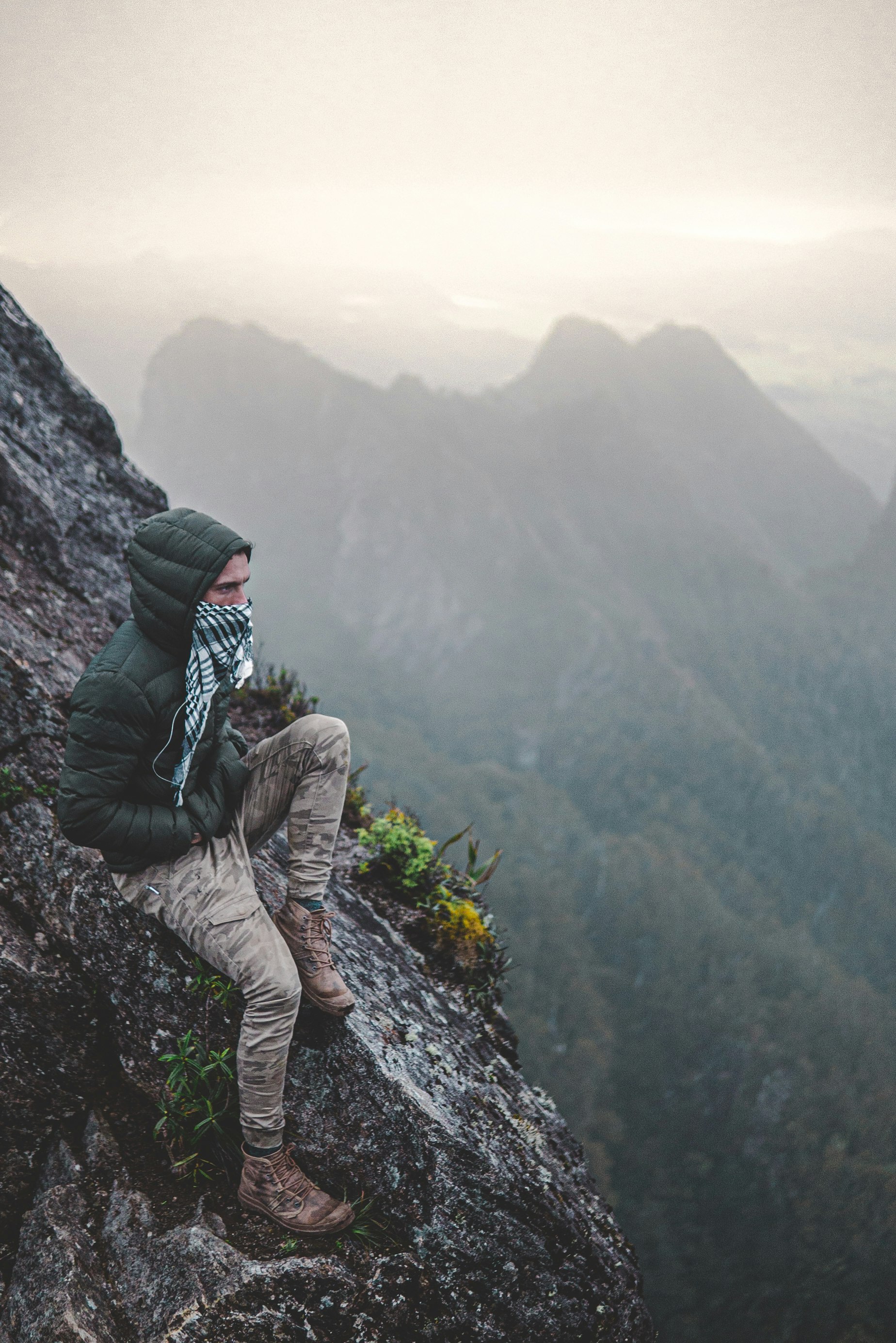 person in green jacket and brown pants sitting on rock during daytime